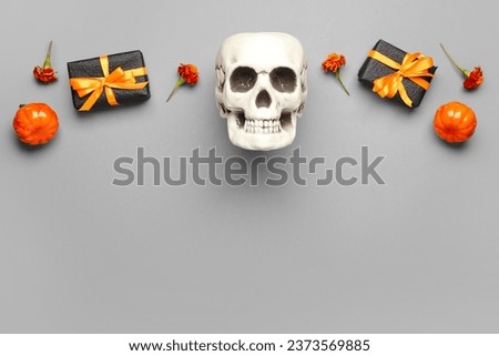 Human skull with marigold flowers, pumpkins and gift boxes on grey background