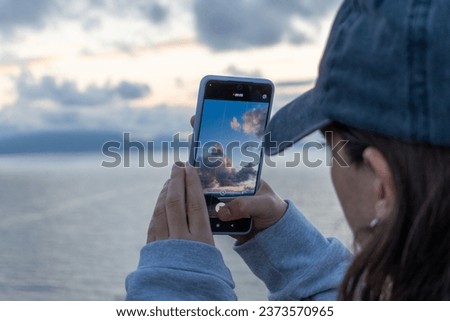 A beautiful view of a woman taking a picture of the sky at the beach with her cell phone