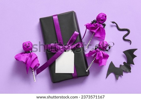 Sweet lollipops with gift box, paper bat and snake for Halloween party on lilac background