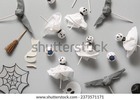 Sweet lollipops with jelly eyes, broom and paper cobweb for Halloween party on grey background
