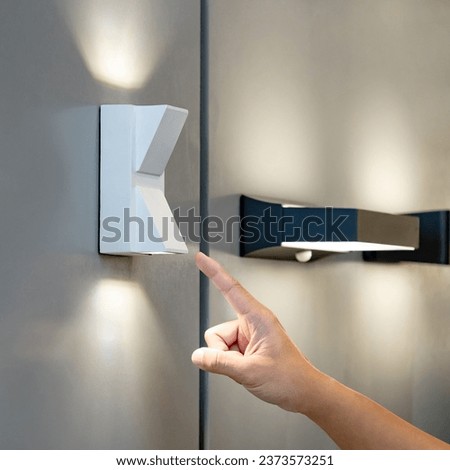 Designer hand pointing at sample of exterior LED wall lamp in home design store. Modern white uplight and downlight light fixture mounted on wall for outdoor lighting Royalty-Free Stock Photo #2373573251