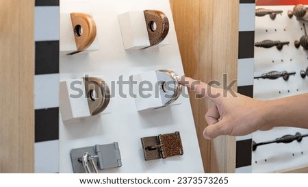Designer hand pointing at fixed metal latch padlock staple on door hardware catalog in home design store. Stainless steel padlock hasp and staple collection. Door fitting part for safety and security Royalty-Free Stock Photo #2373573265