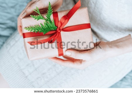 Female hands holding gift handcrafted box thoughtfully wrapped in eco-friendly packaging with with red ribbon bow. Sustainable and eco conscious living concept. top view. High quality photo