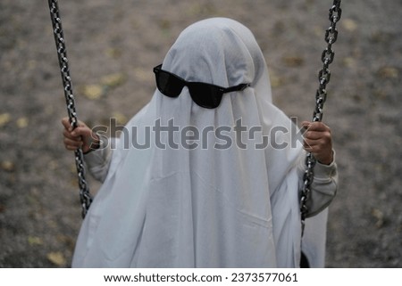 Funny Halloween Kid Concept, little cute child with white dressed costume halloween ghost scary with sunglasses, Ghost costume for Halloween concept.  A ghost of a child under a white sheet.