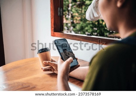 A woman takes a picture of a paper coffee cup in hand with her smartphone while sitting at a coffee shop.