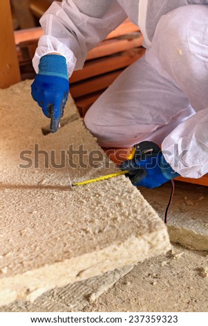 Man installing thermal insulation layer under the roof - using mineral wool panels, closeup