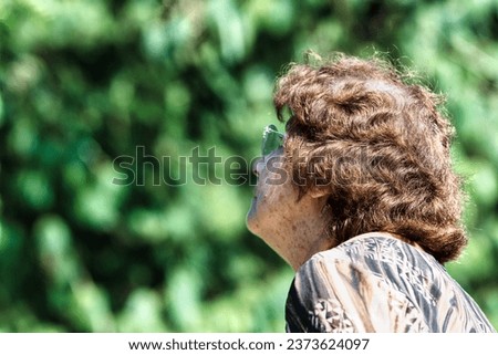 With sun-drenched woods in the background, an aged woman looks skyward. Her chunky glasses are noticeable, and her sparse hair reveals a '50s perm and gray roots, echoing Marilyn Monroe's era