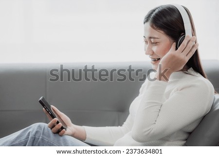 Asian woman surfing social media with headphones using laptop at home on sofa