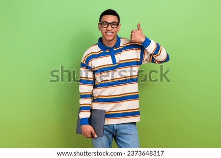 Photo portrait of nice young male showing thumb up hold netbook college dressed stylish striped garment isolated on green color background