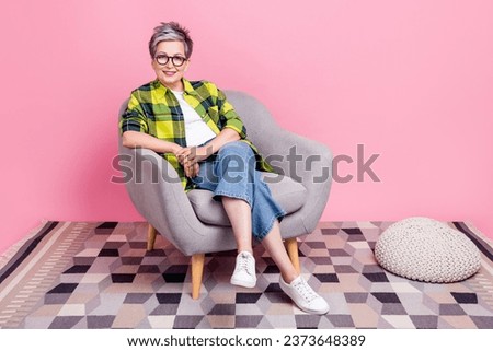 Full size photo of pleasant good mood person dressed plaid shirt siting on armchair on consultation isolated on pink color background