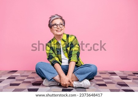 Full size photo of senior person with short hair dressed plaid shirt sitting on floor look empty space isolated on pink color background