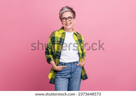 Photo of good mood nice retired woman with short hairstyle wear checkered shirt hold arms in pockets isolated on pink color background