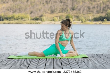 Fitness and lifestyle concept. Young sports woman stretching muscles in a park in front of the lake. Athletic woman stretching. 