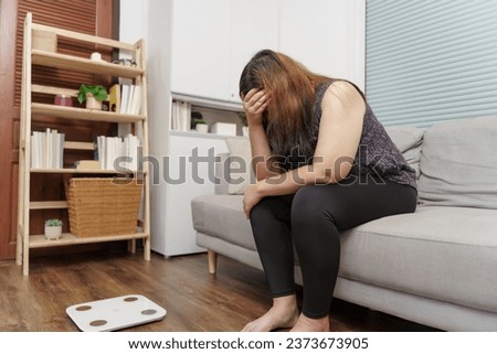 Sad woman with fat upset bored of dieting Weight loss fail  Fat diet and scale sad asian woman on weight scale at home weight control. Royalty-Free Stock Photo #2373673905