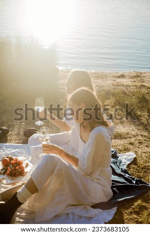 Young beautiful women of 25 years old on an autumn picnic near the lake. Glass of white wine, pastries. Happy models chatting merrily.