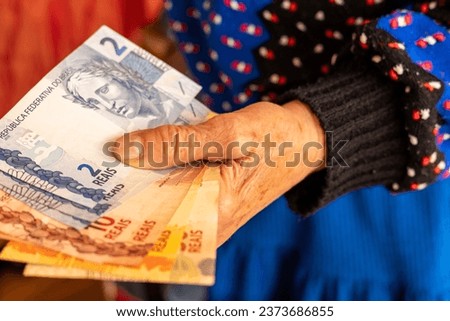 Brazilian money, a pensioner holds several reais banknotes in her hand, Financial problems of seniors, low pensions in Brazil Royalty-Free Stock Photo #2373686855