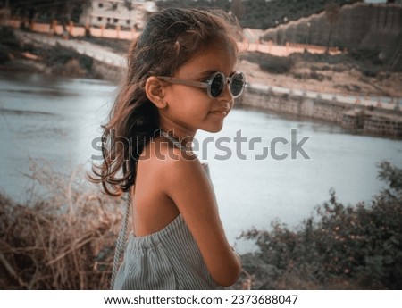 Ai photo simple concept idea with editing raw filter effect.Little girl wearing black eyeglass.White color cloth and hand sitting near pond.