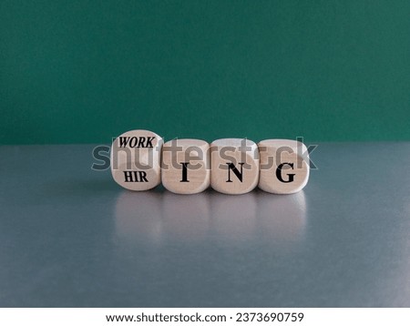 Hiring and working symbol. Turned a wooden cube and changes the word Hiring to Working. Beautiful green background, grey table. Copy space. Business, hiring and working concept.