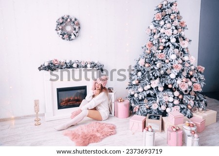 teen in warm knitted winter clothes sits by the fireplace and Christmas tree with gifts. cozy room.