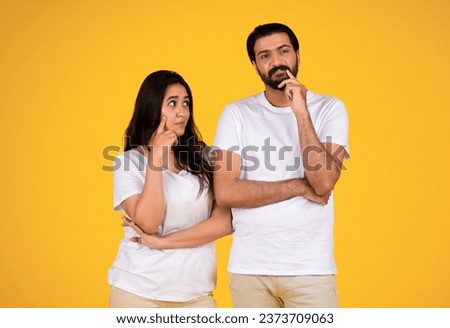 Thoughtful young couple isolated on yellow studio background, both looking contemplative. Expressions serious yet calm, indicating deep thought or concern, creating somber atmosphere Royalty-Free Stock Photo #2373709063