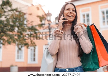 Happy smiling woman holding paper bags with clothes she bought on sales and talking on phone with best friend about new gossips.