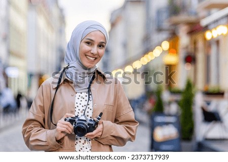 Portrait of young beautiful Muslim woman in hijab, tourist walking in evening city with camera, woman traveling to different countries