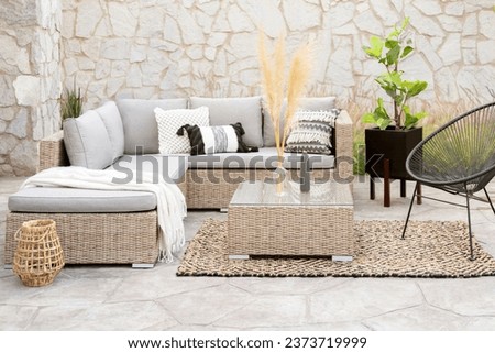 Spring Patio Furniture Set with Rattan Sectional Sofa, Decorative Pillow Covers, Wicker Patio Chairs, and Rattan Coffee Table, on a Botanical Area Rug in an Outdoor Living Space, Decorative Stone Wall Royalty-Free Stock Photo #2373719999