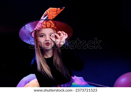 Little girl dressed as a witch with pumpkin on a dark background in the light of multi-colored spotlights
