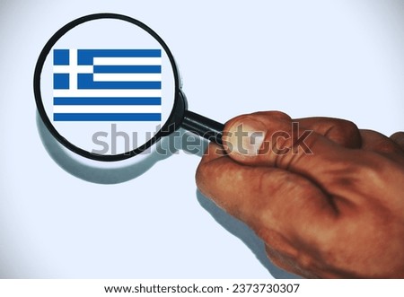 Hand holding a Magnifier glass showing the  Greek Flag .