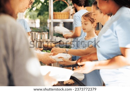Image showcasing charity workers at outdoor food bank, serving the needy homeless people, providing support and alleviating hunger. Volunteers distributing meal rations to poor individuals. Royalty-Free Stock Photo #2373772379