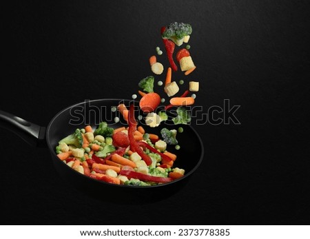 Falling sliced vegetable mix on a frying pan. Flying down frozen vegetables on black background. Natural organic food. Copy space.