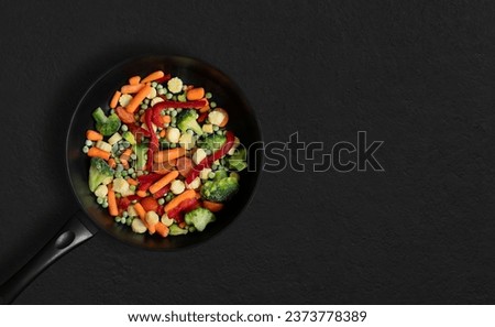 Frying pan with sliced frozen vegetables mix on black background. Vegetable mix salad. Top view, flat lay. Copy space.