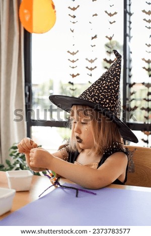 A cute girl in a witch costume makes a funny spider for Halloween with her own hands. The concept of children's crafts for Halloween