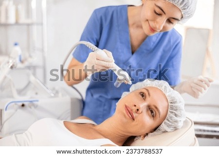 Young female patient undergoing facial skin ionization procedure using ion airbrush pen to rejuvenate and improve overall condition of skin .. Royalty-Free Stock Photo #2373788537