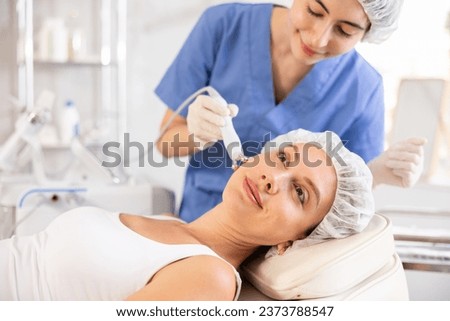 Young woman receiving facial radiofrequency procedure stimulating collagen production resulting in tightened and firmed skin. Modern hardware cosmetology Royalty-Free Stock Photo #2373788547