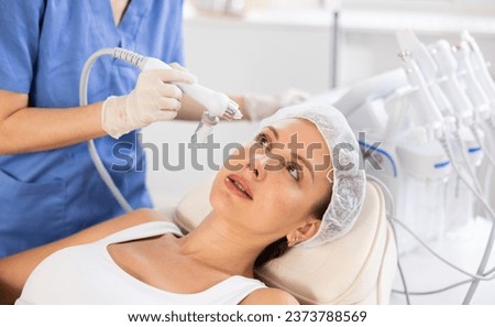 Young female patient undergoing facial skin ionization procedure using ion airbrush pen to rejuvenate and improve overall condition of skin .. Royalty-Free Stock Photo #2373788569