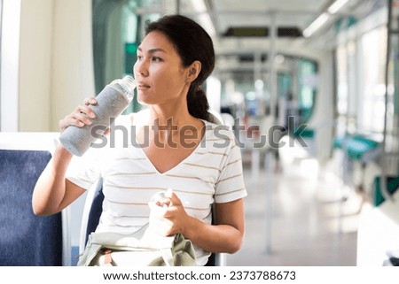 Asian woman sitting in tram with bottle of water in hand. Royalty-Free Stock Photo #2373788673