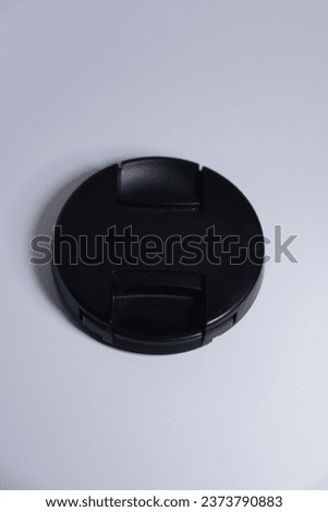 The photo depicts an isolated black lens cap against a white background.