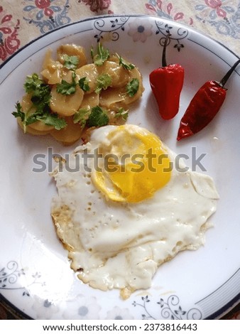 This is a picture in which some food items are placed on a plate including half fried egg aloo curry and some chillies which are very delicious to eat.