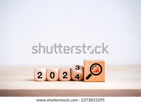 2024 happy new year with new business trends concepts. Flipping the 2023 to 2024 year calendar and magnifying glass with growth graph icon on big wooden cube blocks on wood table on white background.