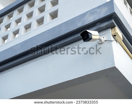 Old white CCTV camera hanging at the corner at the outdoor of modern concrete building.