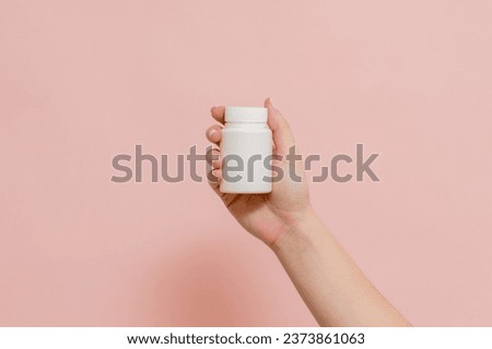 Plastic bottle (tube) in hand on a pink background. Packaging for vitamins, tablets or capsule, or supplement Royalty-Free Stock Photo #2373861063