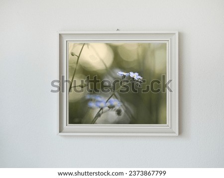 A realistic image of a white wooden picture frame filled with a photo of a blue flower hanging on a white wall.