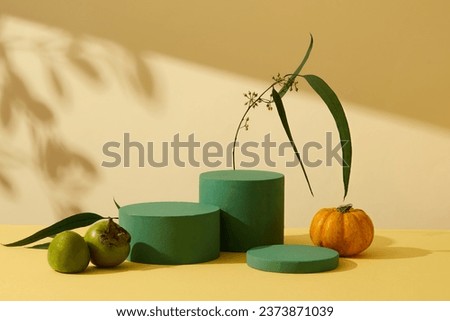 Minimalist empty display product presentation scene with Autumn theme. Three green cylinder podiums displayed on yellow background with pumpkin and green persimmons. Front view