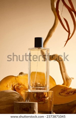 Front view of glass perfume bottle displayed on transparent podium, behind are slices of pumpkin, dry twig and dry leaves on beige background. Advertising photo