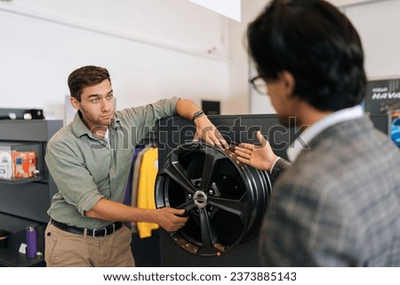 Back view of professional salesman in business suit talking about characteristic of alloy wheel rims product to customer male came to look at assortment, represented in auto service shop. Royalty-Free Stock Photo #2373885143