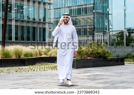 Arab middle-eastern man wearing emirati kandora traditional clothing in the city - Arabian muslim businessman strolling in urban business centre. Royalty-Free Stock Photo #2373888343