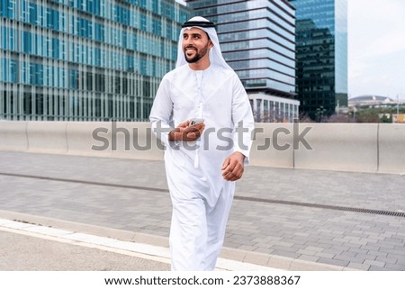 Arab middle-eastern man wearing emirati kandora traditional clothing in the city - Arabian muslim businessman strolling in urban business centre. Royalty-Free Stock Photo #2373888367