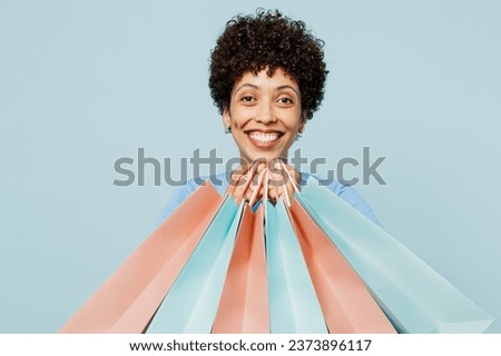 Young woman of African American ethnicity wearing casual clothes hold in hand paper package bags after shopping isolated on plain light pastel blue cyan background. Black Friday sale buy day concept