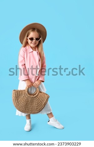 Stylish little girl with bag on blue background